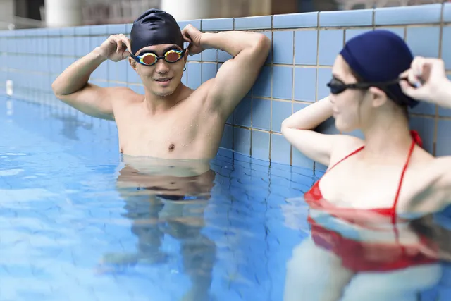 Two adults in goggles and swim caps at the pool wall before a swimming class