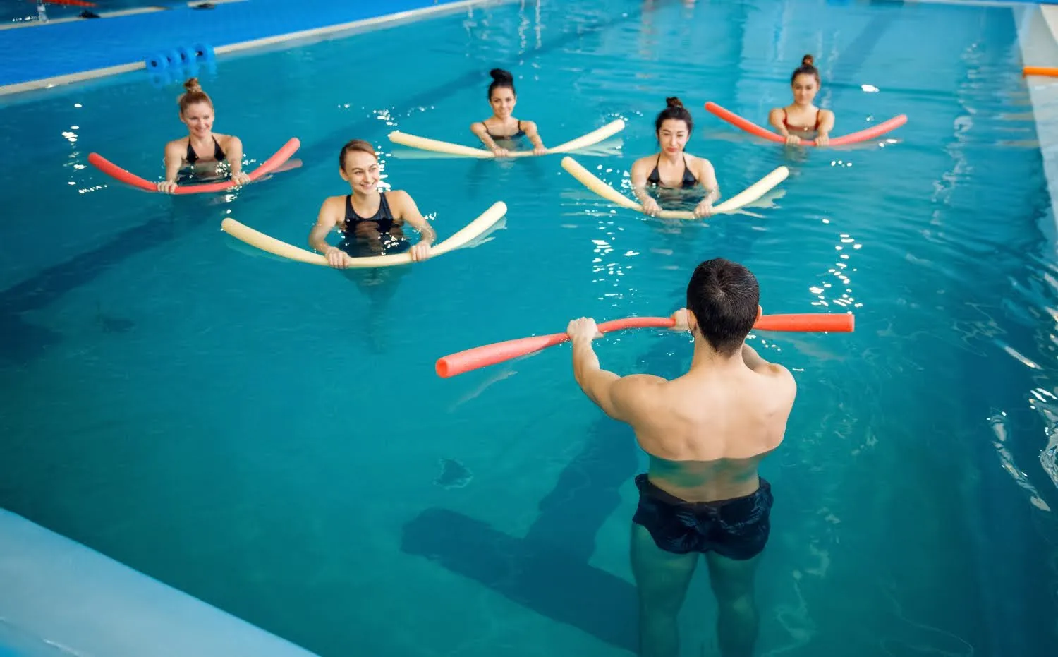 Adults in an aqua fitness class with pool noodles