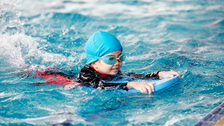 Boy in a swim cap swimming with a kickboard