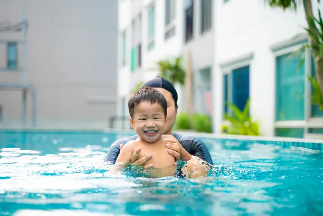 Swimming coach holding a smiling toddler in the pool
