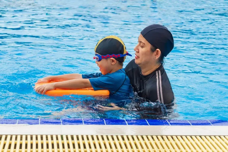 Coach teaching a boy to kick with a foam float