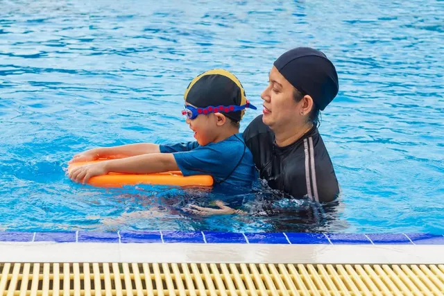 Coach teaching a boy to kick with a foam float