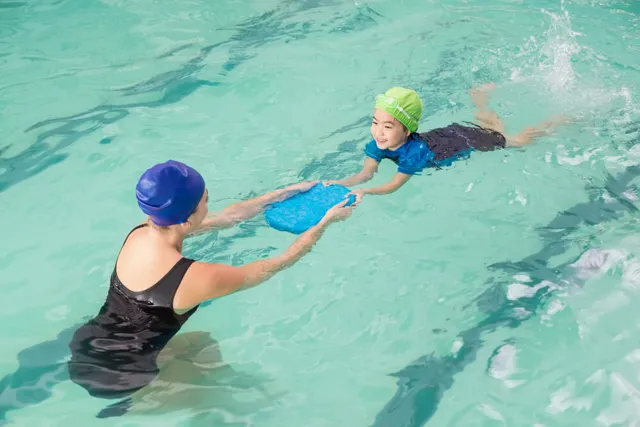 Coach teaching a little boy to swim with a kickboard