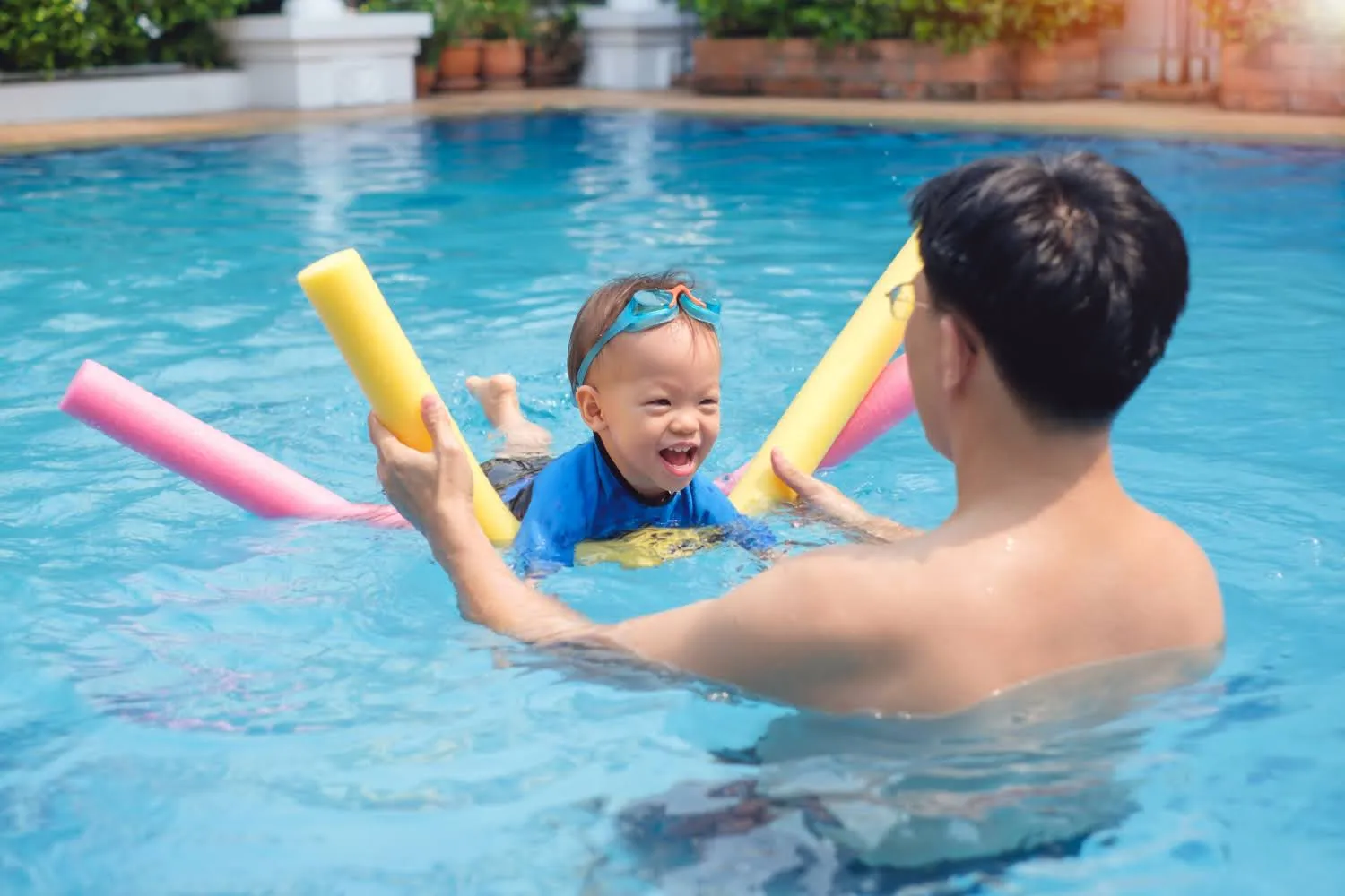 Coach teaching a toddler to swim with pool noodles