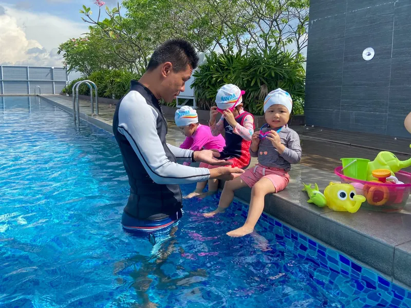 Coach with three toddlers at the poolside in a baby swimming lesson