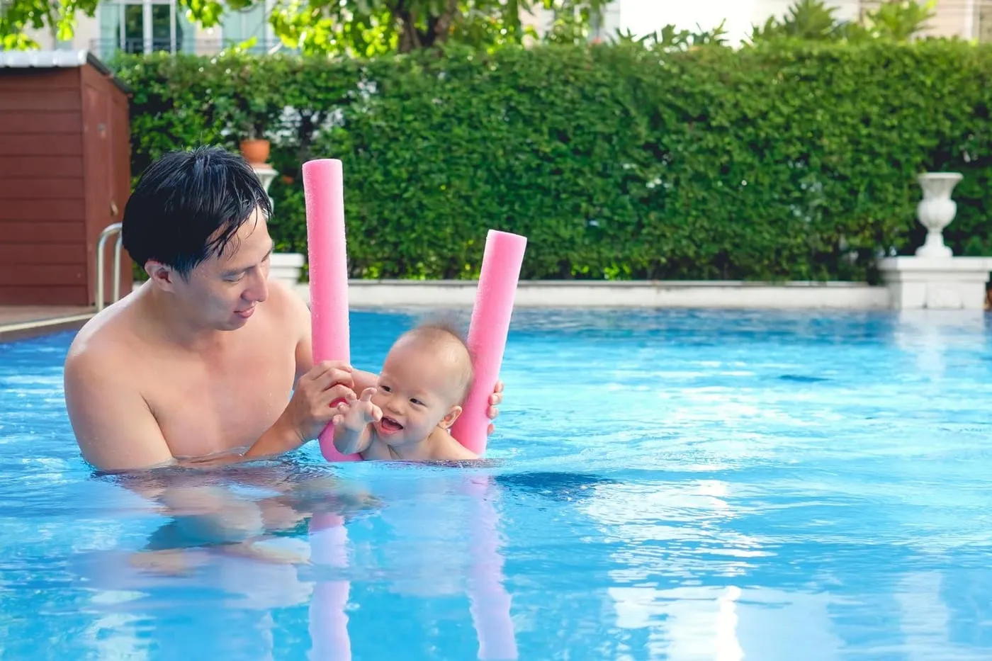 Father holding a baby between pool noodles