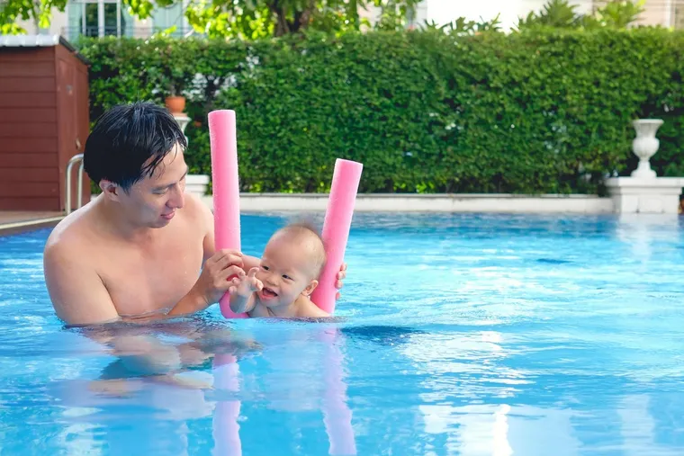 Father holding a baby between pool noodles
