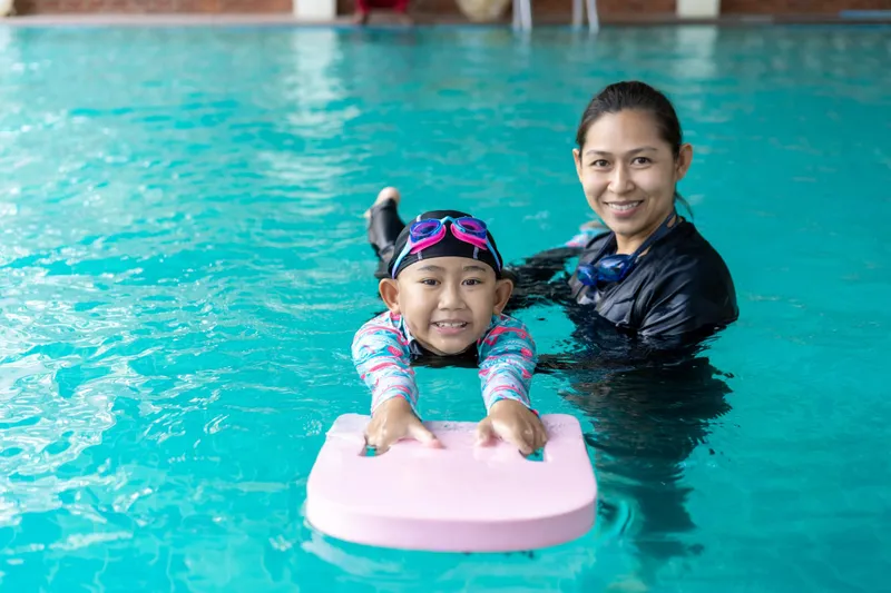 Female swimming coach with a girl on a kickboard