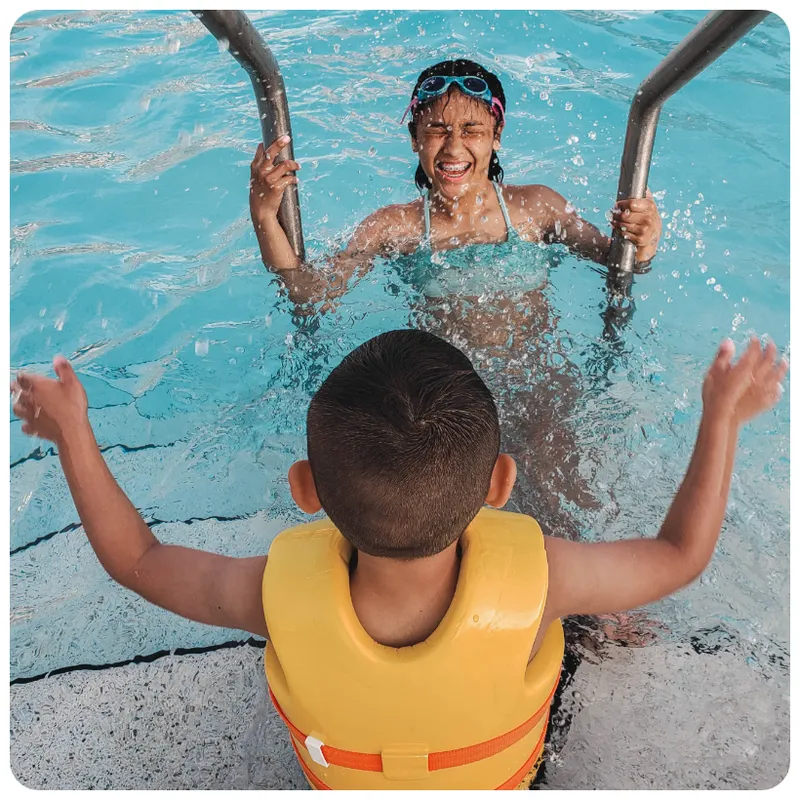 Girl on the pool ladder and a boy in a life vest