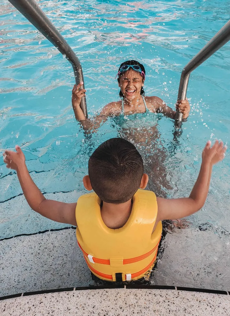 Girl on the pool ladder and a boy in a life vest