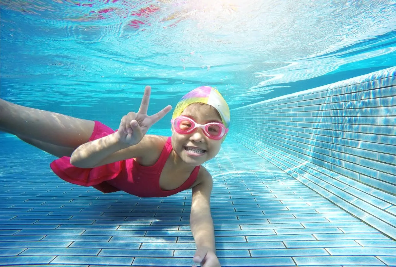 Girl swimming underwater making a peace sign
