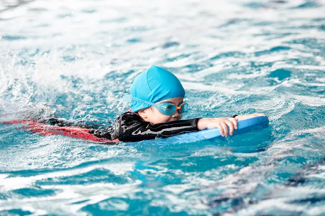 Girl in a swim cap swimming with a kickboard