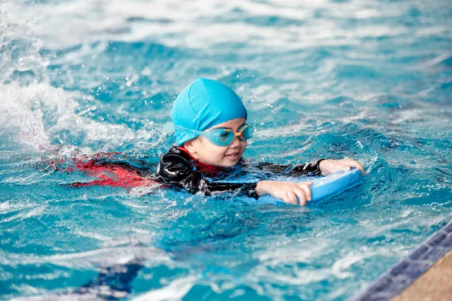 Girl in a swim cap swimming with a kickboard