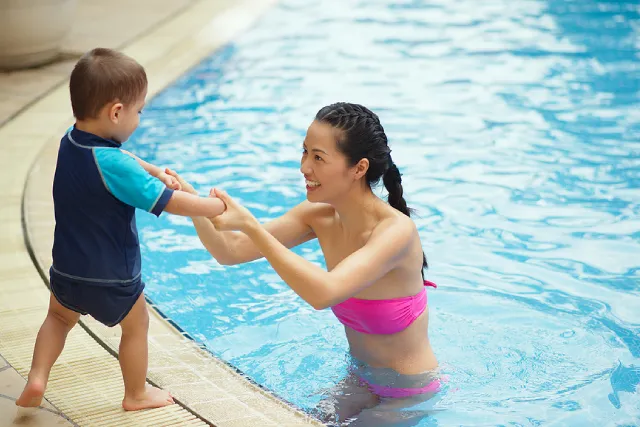 Mother helping a nervous toddler into the pool