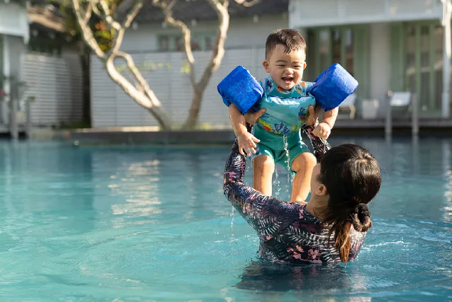 Mother lifting a toddler wearing arm floats in a pool