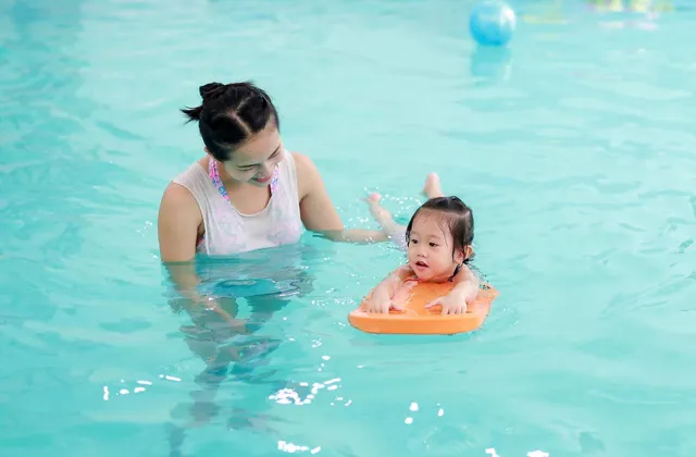 Mother teaching a toddler to swim with a float