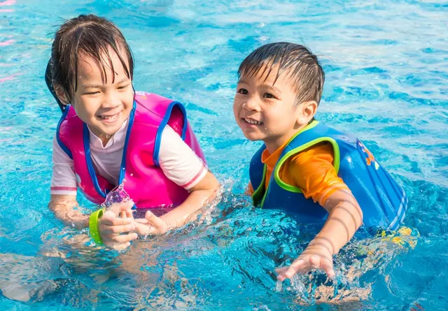 Two siblings in life jackets playing in a pool