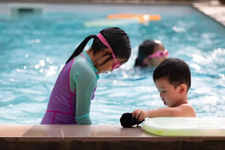 Siblings playing at the pool edge with a kickboard