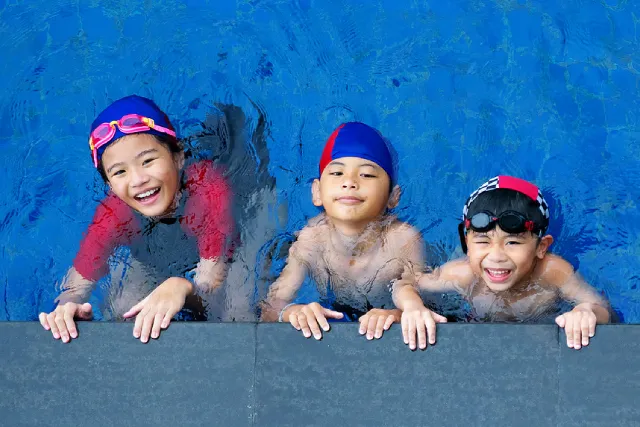 Three kids in swim caps at the pool edge